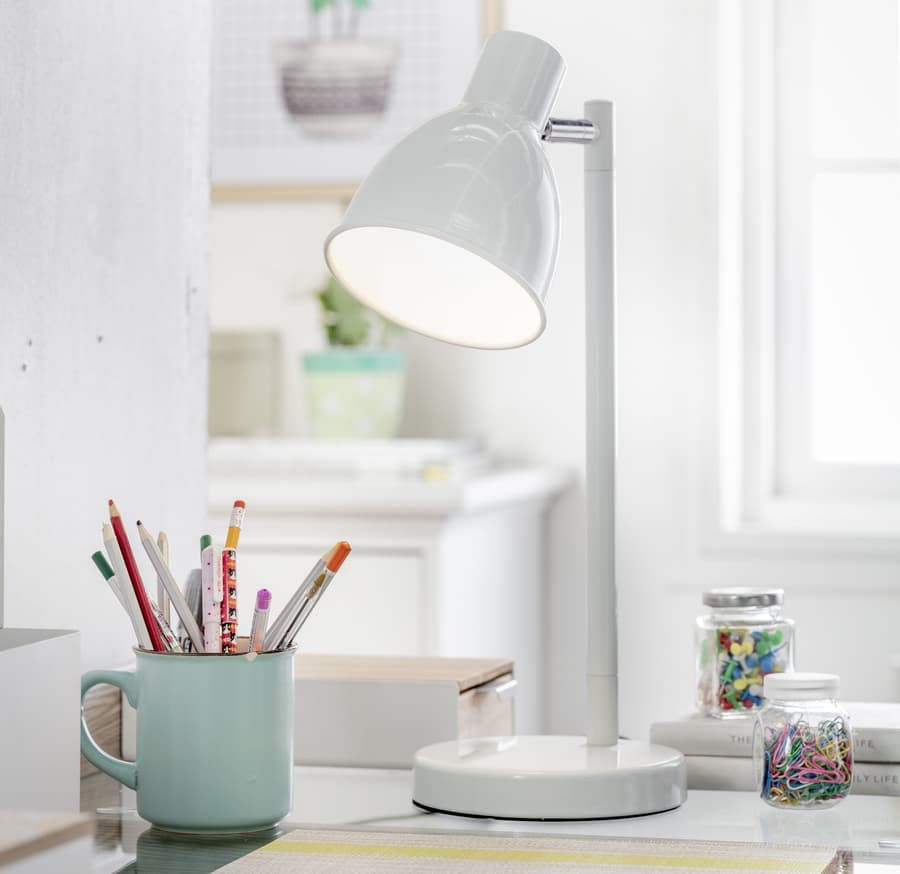 Lámpara de escritorio blanca encendida durante el día, mientras entra luz natural por la ventana.