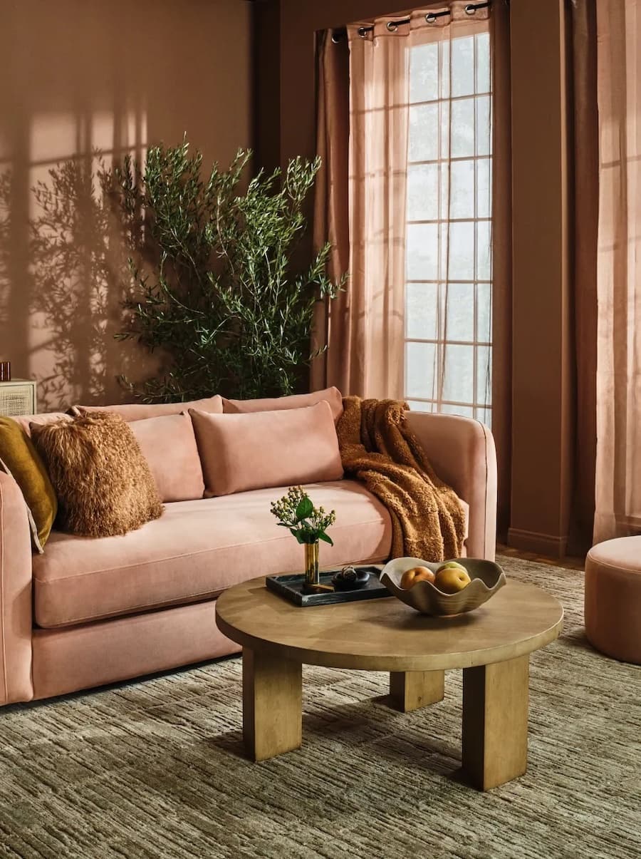 Living de estilo clásico de color Pantone 2025, Mocha Mousse. Tiene un sofá, paredes y cortinas cafés, mesa de centro redonda y una gran alfombra