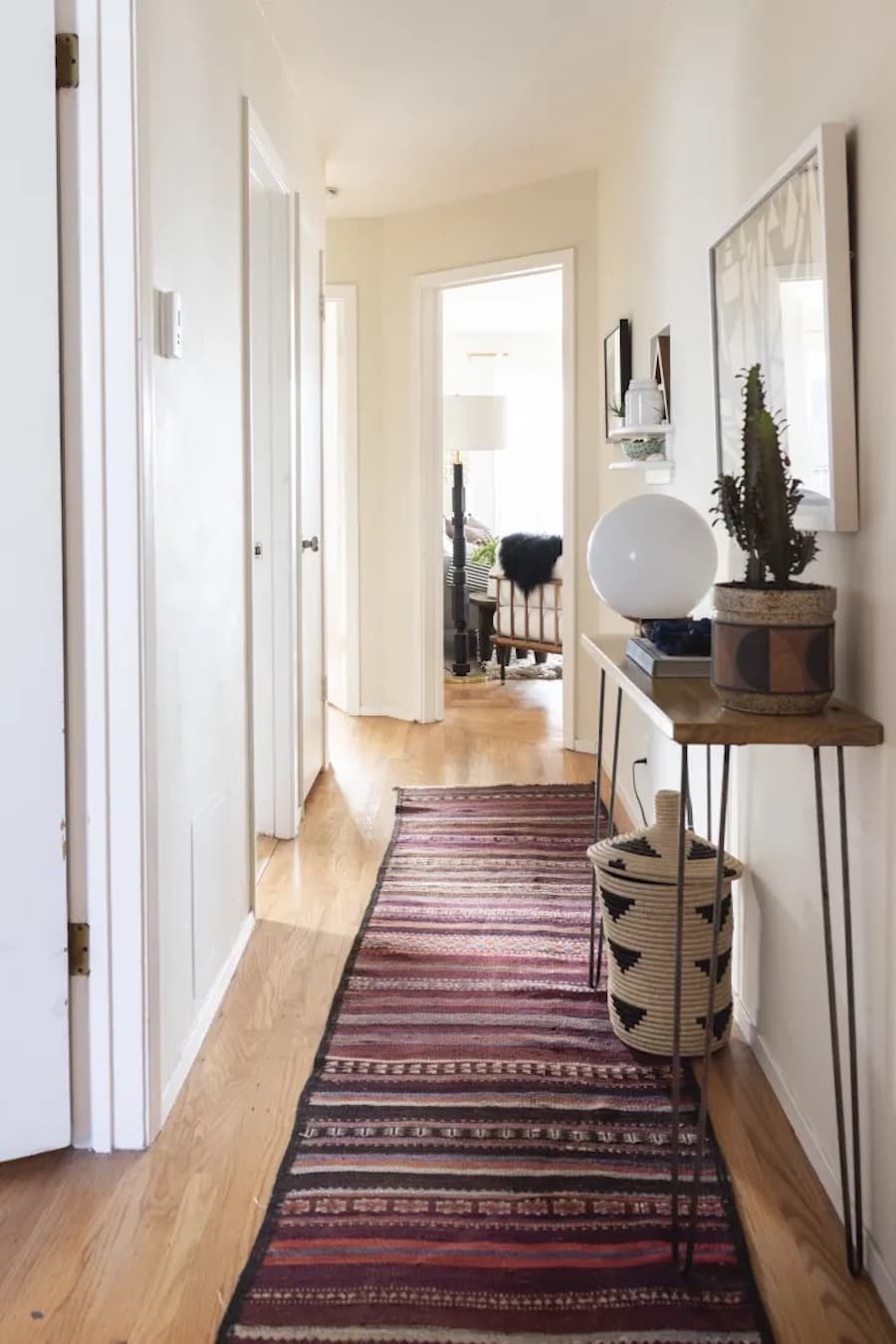 Pasillo estrecho y largo con una alfombra estilo kilim en tonos cálidos. Hay un arrimo de madera con adornos y cuadros en el muro.