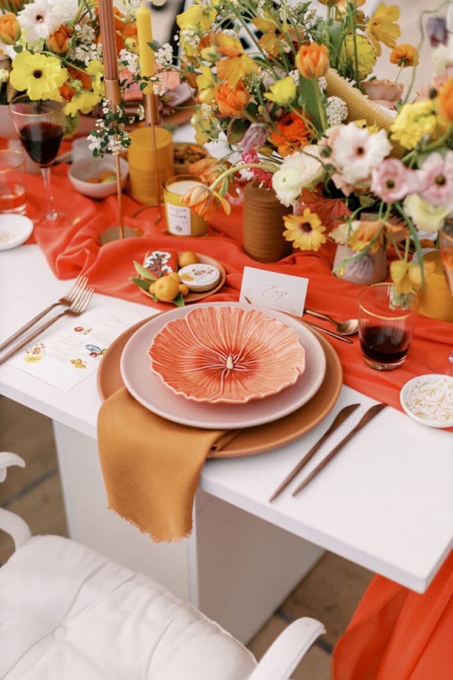 Mesa con vajilla combinada. Mesa blanca con camino de mesa rojo. Puesto con plato grande café, sobre él un plato rosa y arriba un plato con forma de flor, color damasco.