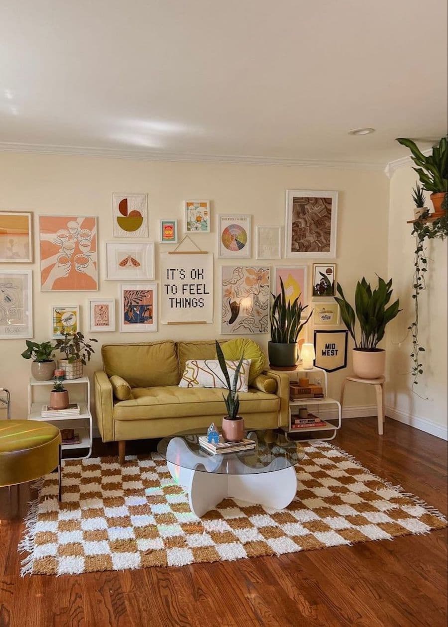 Living con alfombra cuadrillé blanco con café. Mesa de centro redonda, con base de vidrio y sillón color verde, estilo vintage. Pared con muro galería y plantas.