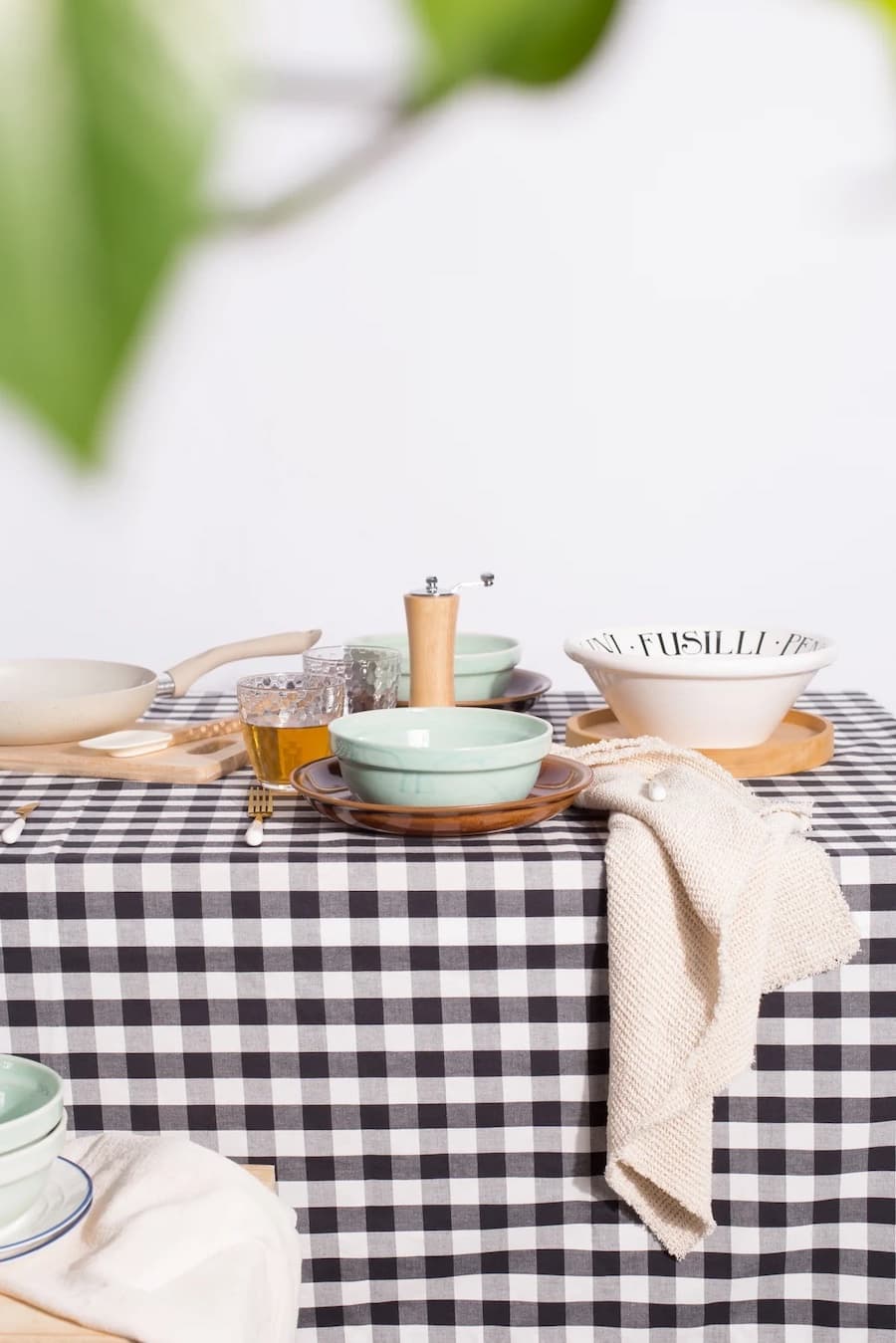 Mesa con mantel cuadrillé blanco con negro. Sobre la mesa hay vajilla color blanco, menta y platos de madera.