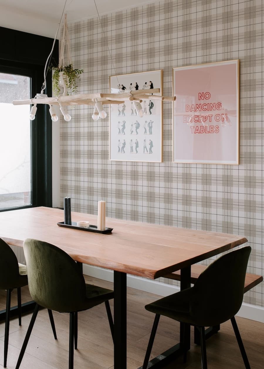 Comedor con papel mural estampado cuadrillé, en tonos beige y café claro. Mesa de madera, sillas con tapiz y una banqueta junto al muro.