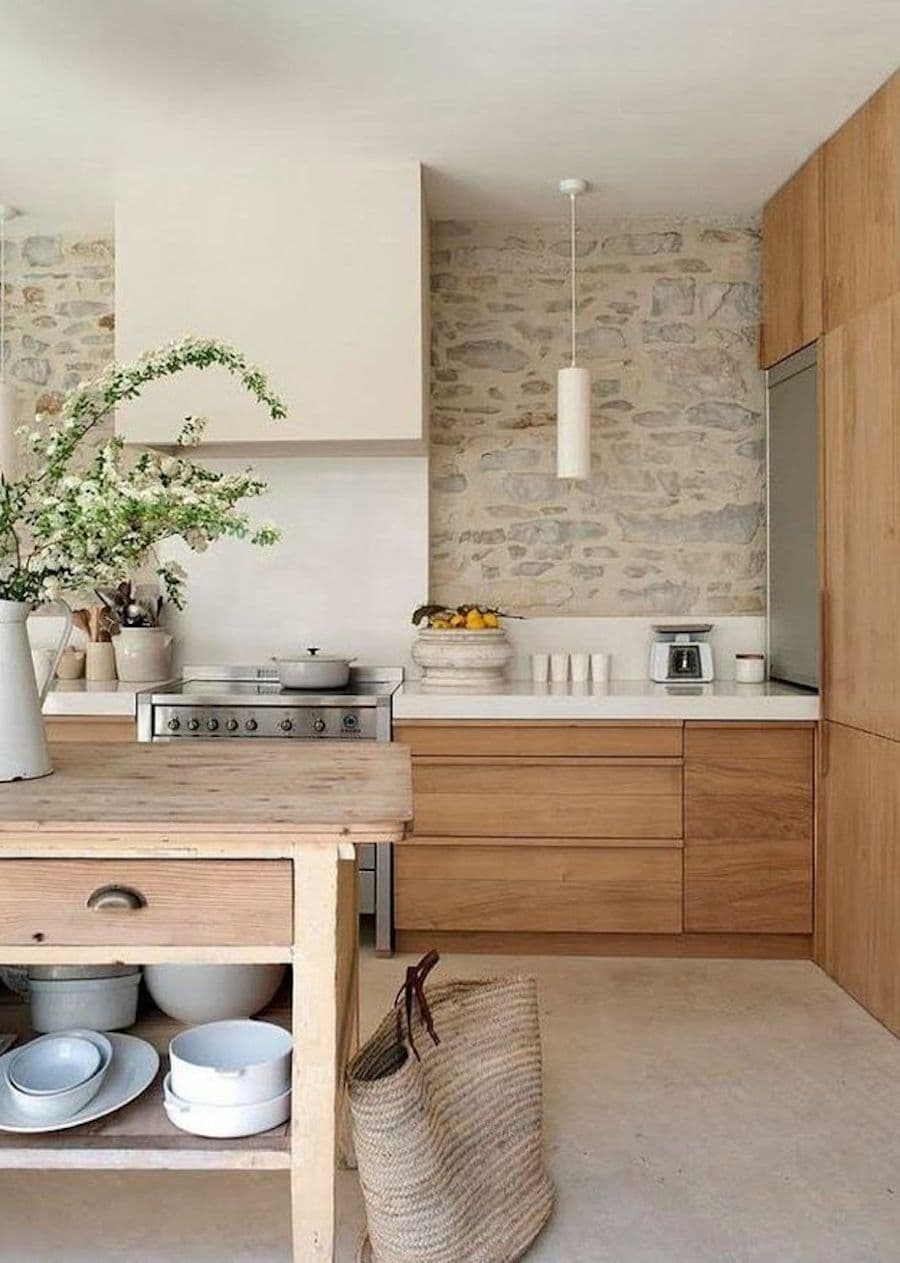 Cocina con un muro de piedra, muebles de madera y cubierta blanca.