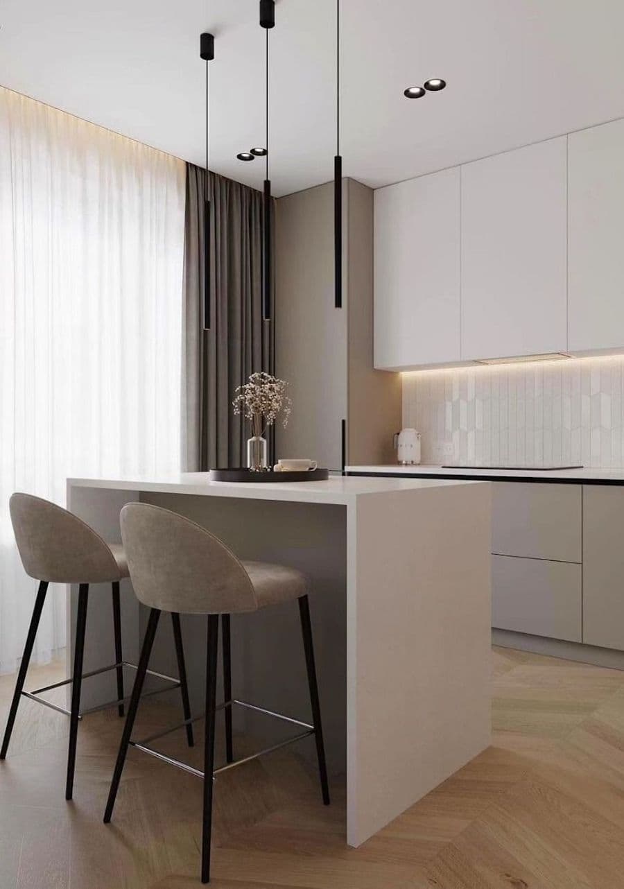 Cocina moderna con muebles color greige. Isla greige con dos pisos altos. Lámparas colgantes minimalistas, negras. Gran ventanal con visillo y cortina gris.