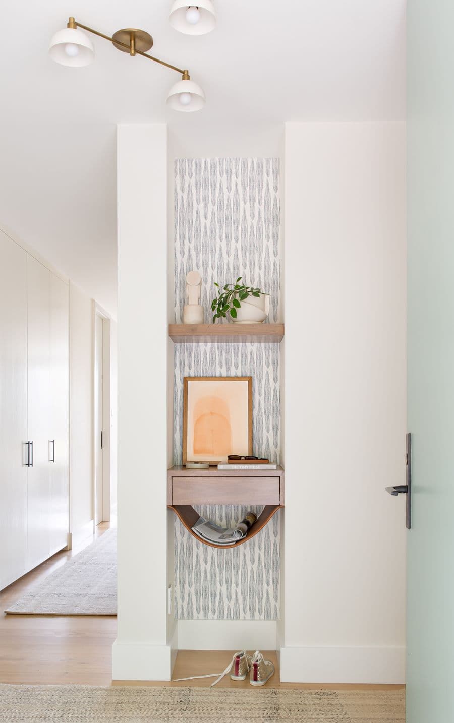 Recibidor pequeño con papel mural, dos repisas flotantes y una pequeña hamaca de cuero para poner revistas.