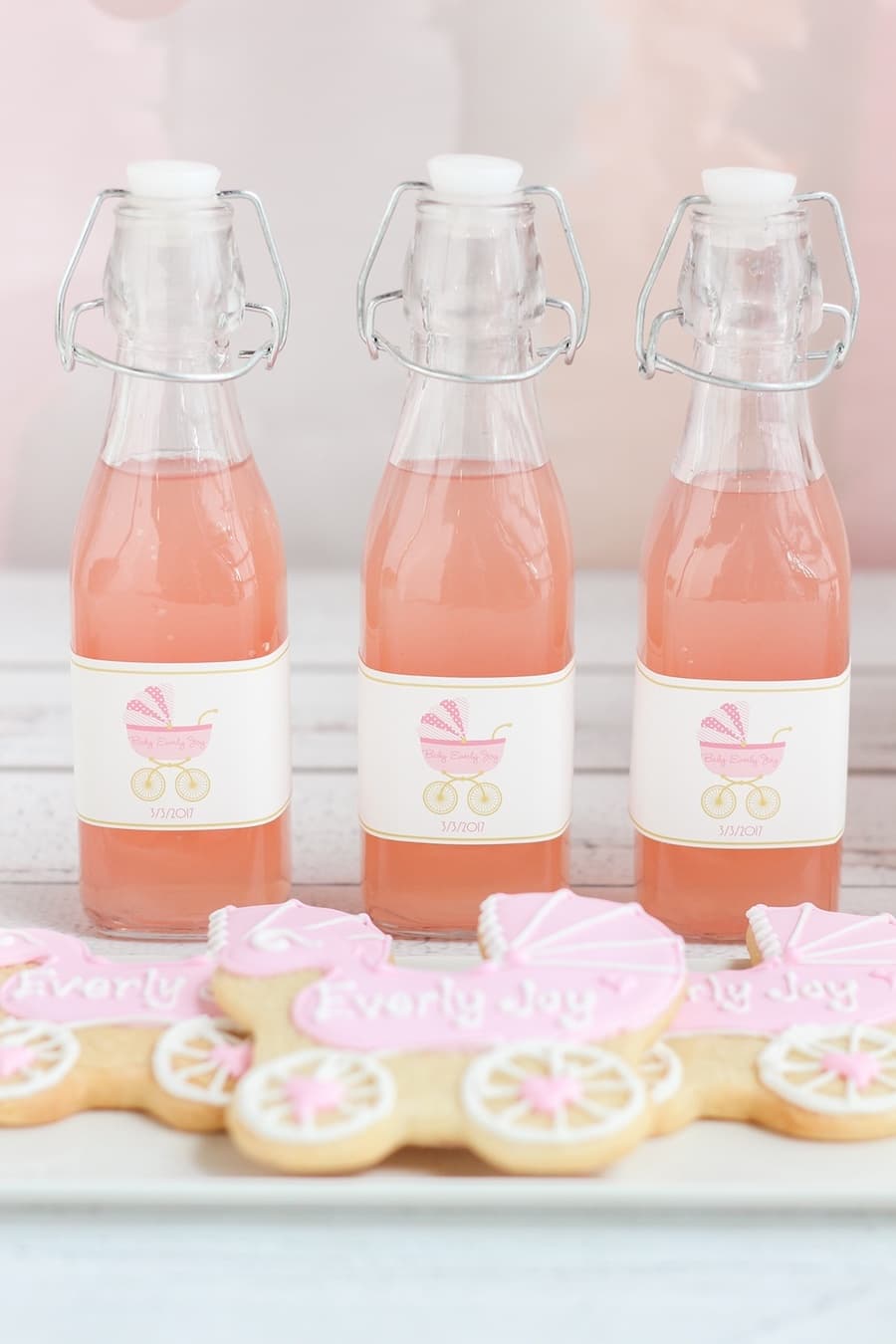 Galletas y botellas en tonos rosa personalizadas para un baby shower, con un diseño de coche antiguo.